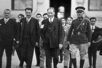Mustafa Kemal Atatürk, yanında askeri üniformalı yaveri ve sivil giyimli heyeti ile birlikte yürüyor.
